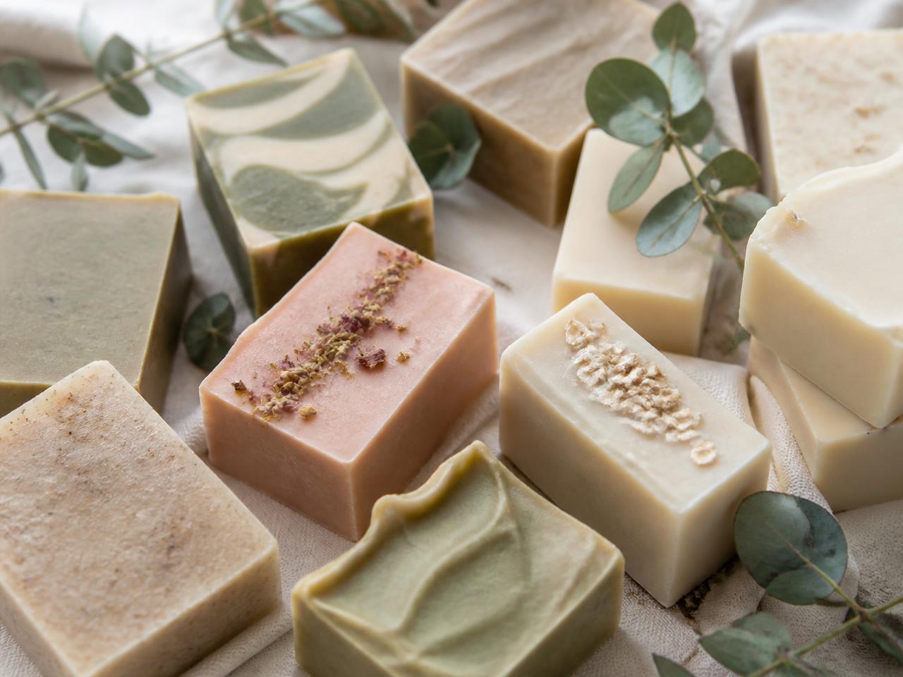Composição com diversos sabonetes artesanais em tons de oliva, creme e rosa sobre tecido claro